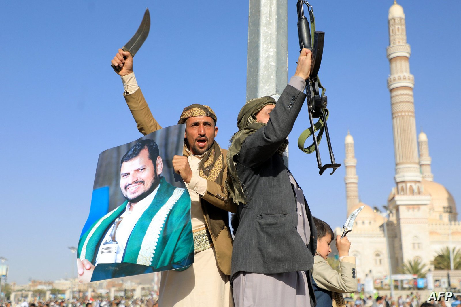 Huthi fighters, one holding a portrait of Huthi leader Abdul Malik al-Houthi (L), brandish their weapons during a protest following US and British forces strikes, in the Huthi-controlled capital Sanaa on January 12, 2024 amid the ongoing battles between Israel and the militant Hamas group in Gaza. US and British forces struck rebel-held Yemen early on January 12, after weeks of disruptive attacks on Red Sea shipping by the Iran-backed Huthis who say they act in solidarity with Gaza. The pre-dawn air strikes add to escalating fears of wider conflict in the region, where violence involving Tehran-aligned groups in Yemen as well as Lebanon, Iraq and Syria has surged since the Israel-Hamas was began in early October. (Photo by MOHAMMED HUWAIS / AFP)