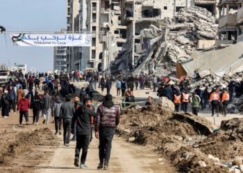 People gather by a banner welcoming people near the rubble of a collapsed building along Gaza's coastal al-Rashid Street for people to cross from the Israeli-blocked Netzarim corridor from the southern Gaza Strip into Gaza City on January 26, 2025. Israel said on January 25 it would block the return of displaced Palestinians to their homes in northern Gaza until Arbel Yehud, one of the hostages taken captive during the October 7, 2023 attacks, is released. Hamas sources said that Yehud was "alive and in good health", and would be "released as part of the third swap set for next Saturday", on February 1. (Photo by Omar AL-QATTAA / AFP)