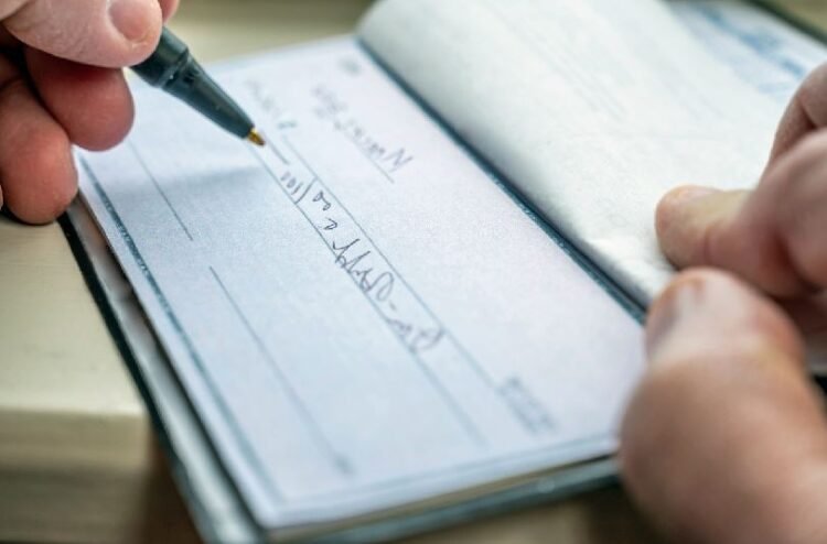 main qui remplie un cheque chequier portefeuille