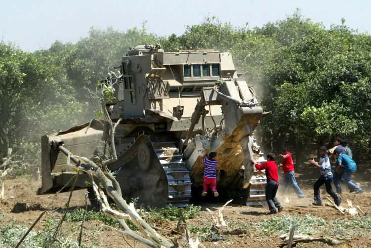 BEIT HANON, GAZA STRIP - MAY 19:  Palestinian boys throw stones at an Israeli tank as it destroys an orange farm May 19, 2003 at Beit Hanoun town in the northern Gaza Strip. Israeli troops continued the seizure of Beit Hanoun in an effort to stop Palestinian militants from firing rockets across the fence into Israel. Palestinian security sources stated that Israeli bulldozers destroyed four more houses and part of a mosque in the northern town of Beit Hanun. The Israelis also razed approximately 49 acres (200 dunams or 20 hectares) of agricultural land in the area which has been the site of heavy military activity since the end of last week. Israeli troops entered the northern Gaza Strip the morning of May 15 in a bid to further dismantle the infrastructure of militant groups and prevent rocket attacks on Israeli targets, many of which are launched from fields around the area.  (Photo by Abid Katib/Getty Images)